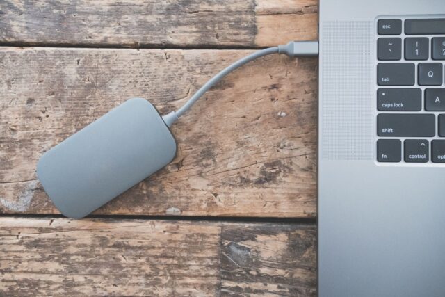 Hard disk extern conectat la un laptop, pe o masă de lucru ordonată