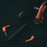 Cabluri audio strânse în colac, cu conectori XLR, jack și RCA așezați pe o suprafață întunecată
