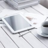 Persoană care citește știri despre tehnologie pe o tabletă, lângă o ceașcă de cafea