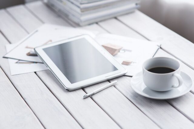 Persoană care citește știri despre tehnologie pe o tabletă, lângă o ceașcă de cafea