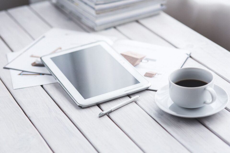 Persoană care citește știri despre tehnologie pe o tabletă, lângă o ceașcă de cafea