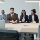 Echipă mică într-un birou luminos, în ședință video cu colegii care lucrează de acasă